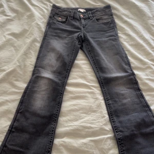Mörkgrå jeans med knappar och fina detaljer från Gina tricot  -  Grå jeans från Gina Tricot i storlek 158 (tall). Jeansen är utsvängda där nere och har coola broderade rosetter på bakfickorna samt kopparfärgade knappar. Klassisk femficksmodell i mjukt denimtyg, perfekt för dig som gillar en stilren look med en twist.
