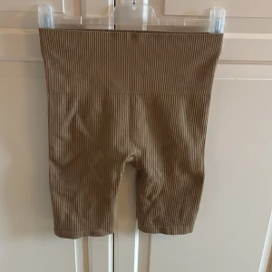 Ribbstickade beige shorts från Röhnisch - Snygga ribbstickade shorts från Röhnisch i en beige färg. De är högmidjade och har en tight passform som sitter skönt mot kroppen. Materialet är stretchigt syntet. Diskret logga framtill i samma ton. Storlek M/L. I fint skick. 