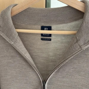 Beige merinoullskofta från Boggi Milano - Stilren beige kofta från Boggi Milano i extra fin merinoull. Modellen har hel dragkedja framtill, klassisk krage och ribbade muddar vid ärmslut och nederkant. Perfekt för lager-på-lager och snygg till både jeans och chinos.