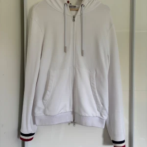Vit Moncler Zip-hoodie tricolor - Moncler Tricolor ziphoodie i vit färg, sitter lite för tight på mig därför jag säljer, har några svarta fläckar som jag inte fått bort i tvätten plus lite där framme. Någon kunnig kanske vet hur man får bort dem!
