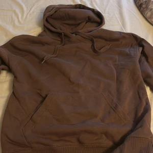 Brun hoodie med huva och magficka - Mysig brun hoodie med stor huva och dragsnören. Tröjan har en klassisk magficka och ribbade muddar vid ärmslut och nederkant. Perfekt för chill dagar eller när du vill ha en avslappnad stil. Tröjan är xxs men stor i storleken så hade passat xs-S också
