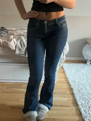 Blå low flare jeans XS - Säljer ett par mörkblå low flare jeans med låg midja och utsvängda ben. Jeansen har klassisk femficksdesign, rå kant nertill och är tillverkade i mjukt denimtyg. Perfekta för dig som gillar en retroinspirerad look med snygg passform.