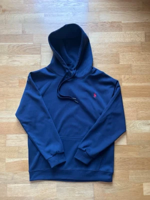 Marinblå Ralph Lauren Hoodie - Mjuk och stilren hoodie i marinblått. Perfekt för vardag eller helg, med praktisk framficka och justerbar huva. Klassisk Ralph Lauren-logga ger en snygg och tidlös look.