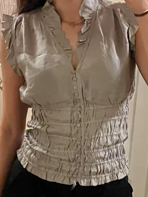 Supersöt volangblus från zara - Söt kortärmad blus med små volanger och smockad detalj nedtill. Storlek S, normal i storlek. Mycker bra skick. Den har även knappar nedtill. 