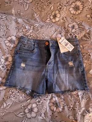 Blå jeansshorts från KappAhl - Säljer ett par klassiska blå jeansshorts från Kappahl med slitna detaljer framtill. Perfekta till sommaren. Säkjet dessa för de aldrig kom till användning.
