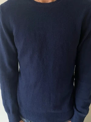 Mörkblå kashmirtröja från J.Lindeberg - Säljer en stilren mörkblå kashmirtröja från J.Lindeberg. Tröjan har rund halsringning, ribbade muddar och lång ärm. Perfekt för dig som vill ha en mjuk och klassisk tröja med premiumkänsla.