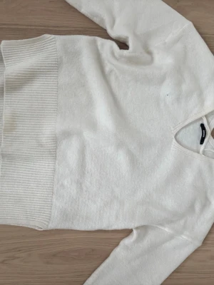 Vit stickad tröja från BikBok - Mysig vit stickad tröja från BikBok i storlek S. Tröjan har ribbade muddar vid ärmslut och nederkant samt en klassisk v-ringning. Perfekt för lager på lager under höst och vinter. Enkel och stilren design som passar till allt.