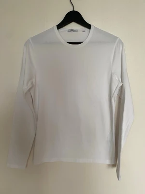  Långärmad t-shirt från Bläck  - Klassisk vit långärmad t-shirt från Bläck i mjuk och stretchig bomullsblandning. Enkel och clean design med rund halsringning, perfekt att styla lager på lager eller bära som den är. Materialet är 95% bomull och 5% elastan.