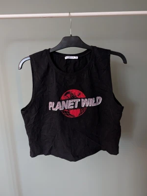 Svart croppad linnetopp Planet Wild - Cool svart croppad linnetopp från Black Story med trycket 'PLANET WILD' i leopardmönstrad text och en röd jordglob på bröstet. Toppen är ärmlös och har en avslappnad passform, perfekt till jeans eller shorts.