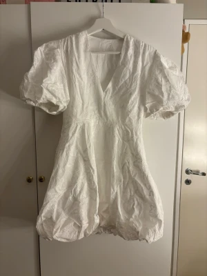 Vit kortklänning med puffärmar - Supersöt vit kortklänning med puffiga ärmar och v-ringning. Klänningen har ett diskret broderat mönster och ballongformad kjol. Perfekt för sommarens alla tillfällen och ger en riktigt trendig look. Köpte som en studentklänning men inte använt den❣️❣️