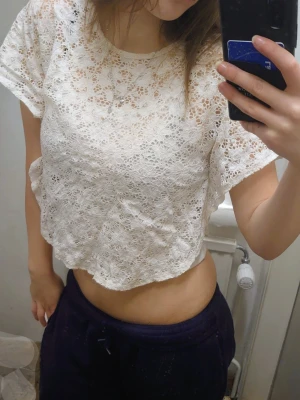 Vit spetsblu - Säljer en söt vit blus med genombruten spets och blommigt mönster. Blusen har bred resår i nederkanten och rund halsringning. Perfekt att styla med jeans eller kjol för en fräsch look.