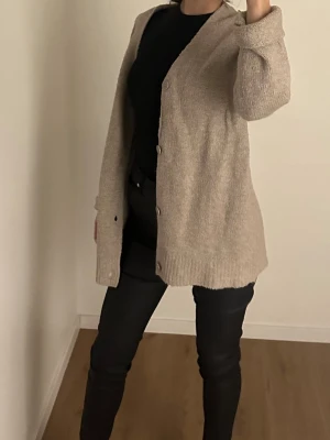 Beige stickad kofta med knappar - Mysig beige stickad kofta med lång ärm och knappar framtill i storlek S passar även XS