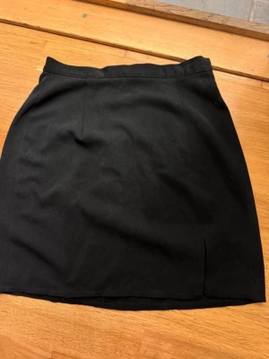 Svart enkel kortkjol - Säljer en svart, stilren kortkjol med rak passform. Kjolen har en klassisk midja och är sydd i ett mjukt tyg som känns bekvämt. Perfekt att matcha med en crop top eller stickad tröja för en clean look.