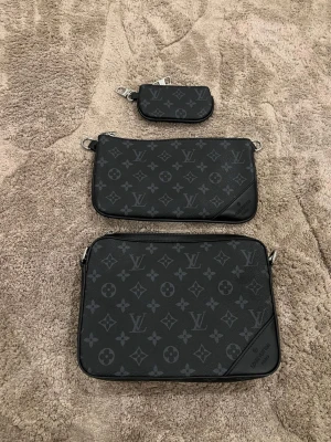  svart axelväska monogram - Säljer en svart axelväska från Vuitton med klassiskt monogrammönster i grått. Väskan har flera delar, inklusive en liten avtagbar plånbok och justerbar axelrem. Tillverkad i skinn med silverfärgade metalldetaljer. Perfekt för dig som vill ha en stilren och lyxig accessoar.