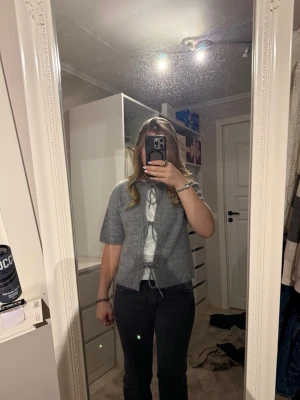 Grå kofta med knyt framtill från Gina tricot❣️ - Säljer en mysig grå kofta med korta ärmar och tre knytband framtill. Koftan är stickad och har en enkel, clean look som passar perfekt till jeans eller kjol. Perfekt för lager på lager under vår och höst.