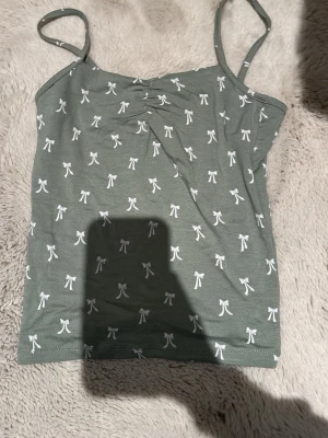 Grön linnetopp med rosettprint XS från Lager 157 - Söt grön linnetopp från Lager 157 i storlek XS. Toppen har tunna axelband och är täckt av små vita rosetter som ger en gullig vibe. Materialet känns mjukt och stretchigt, perfekt för varma dagar eller som layering-piece eller som pyjamas. Har använt en gång sedan bara legat i garderoben, fick hänga med i rensningen.
