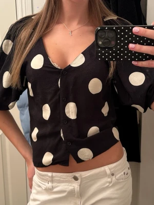 Svart prickig blus med knappar - Snygg prickig vringad topp i väldigt bra skick!