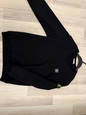 Svart sweatshirt från Stone Island M - Säljer en svart sweatshirt från Stone Island i storlek M. Tröjan har klassisk rund hals, ikonisk patch på ärmen och diskret logga på bröstet. Tillverkad i 100% bomull för skön känsla och stilren look. Perfekt till streetwear eller chill vardagsstil.