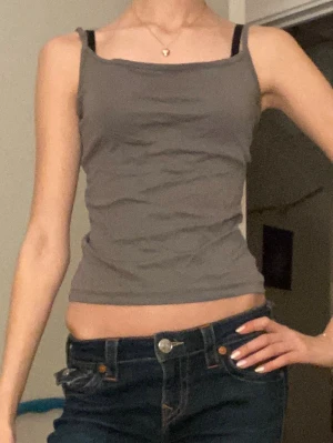 Grå ärmlös linnetopp - Säljer en enkel och stilren grå linnetopp med smala axelband och rak halsringning. Toppen är croppad och har en figurnära passform, perfekt till jeans eller kjol. Materialet känns mjukt och lätt, vilket gör den skön att bära under varma dagar.