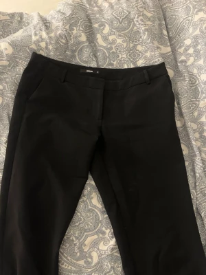 Svarta kostymbyxor från Bik Bok - Klassiska svarta kostymbyxor från Bik Bok med raka ben och bälteshällor. Byxorna har diskreta sidofickor, vävt material som ger en stilren look. Perfekta för dig som gillar enkel och clean stil. Tall längd. Lite längre än lågmidjad 