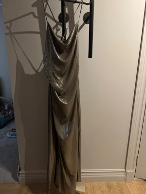 Champagnefärgad långklänning Adoore - Säljer en glansig champagnefärgad långklänning från Adoore med tunna axelband och snygg drapering framtill. Klänningen har öppen rygg med snörning och ett elegant fall. Perfekt för dig som vill sticka ut med en lyxig look.