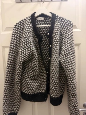 Svartvit rutig kofta Holly & Whyte - Mysig svartvit rutig kofta från Holly & Whyte by Lindex. Koftan är stickad med fluffig känsla, har långa ärmar, svarta ribbade muddar och pärlknappar framtill. Perfekt för lager på lager under kyliga dagar.