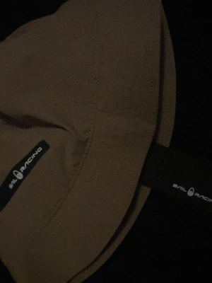 Sail racing sol hatt - Säljer en beige väst från Sail Racing med stilren design och diskret logga på framsidan. Västen har klassisk passform och är tillverkad i ett mjukt material som känns bekvämt. Perfekt för dig som gillar enkel och sportig stil.