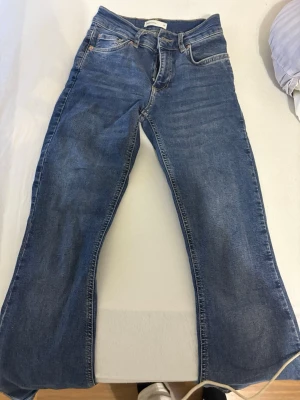 Blå Perfect Jeans från Gina Tricot - Säljer ett par klassiska blå jeans från Gina Tricot, modell Perfect Jeans. De har fem fickor, dragkedja och knapp framtill samt snygga kontrastsömmar. Jeansen har en rak passform och är tillverkade i mjukt denimtyg som sitter skönt hela dagen.