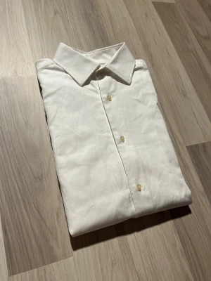 Vit skjorta från Riley Slim Fit - Klassisk vit skjorta från Riley i slim fit-modell. Skjortan har långa ärmar, knappar framtill och en stilren krage. Tillverkad i bomull för en skön känsla och snygg passform. Perfekt för dig som gillar en clean och enkel stil. Se mått på sista sidorna. Skjortan är i utmärkt skick. Hör av er vid frågor!                                                                           Skickas snabbt o välpackat!📦💨