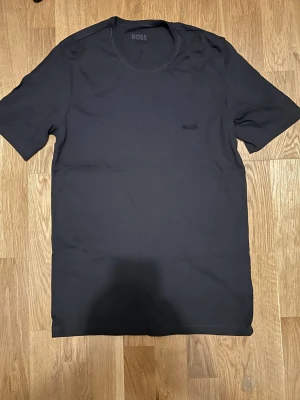 Svart t-shirt från BOSS - Säljer en stilren svart t-shirt från BOSS med diskret logga på bröstet. Klassisk rund halsringning och korta ärmar. Tillverkad i mjuk bomull som känns skön mot huden. Perfekt för dig som gillar minimalistisk och clean stil.