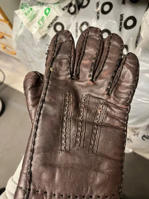 Brun skinnväst med ullfoder - Säljer en mörkbrun väst i mjukt skinn med synliga sömmar och ett varmt, ljust ullfoder på insidan. Västen har klassisk design utan mönster och är perfekt för kyliga dagar. Tillverkad i Kina.