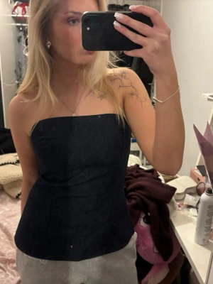 Mörkblå axelbandslös tubtopp - Säljer en stilren mörkblå tubtopp i denim-look. Toppen är axelbandslös och har en enkel, rak skärning. Storleken är L men är från zara som har lite mindre storlekar.