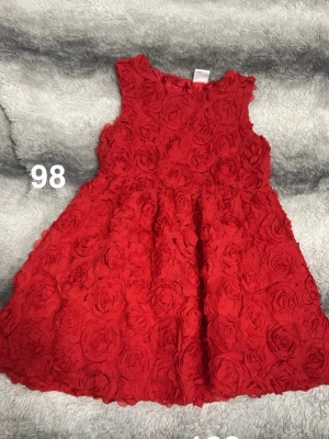 Röd blommig ärmlös klänning - Supersöt röd klänning med 3D-blommor över hela tyget. Ärmlös modell med rund hals och utställd kjol. Perfekt för dig som vill sticka ut med en unik look. Passar till många olika tillfällen!🌸 Fint använt skick. Storlek 98