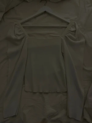 Vit långärmad topp från Dilvin - Säljer en stilren vit långärmad topp från Dilvin med fyrkantig urringning och puffiga axlar. Toppen är stickad och har en clean, minimalistisk look som passar perfekt till jeans eller kjol.