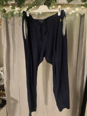 Mörkblå mjukisbyxor från Polo Ralph Lauren - Mörkblå mjukisbyxor från Polo Ralph Lauren med gul broderad logga vid fickan. Byxorna har dragsko i midjan och är tillverkade i mjukt bomullsmaterial. Perfekta för chill dagar hemma eller när du vill vara extra bekväm.