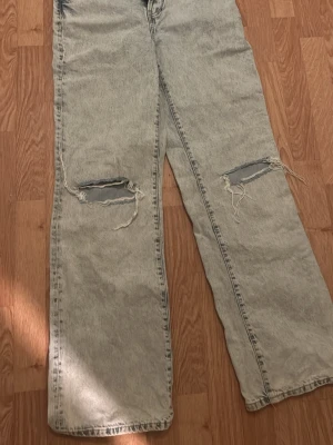 Ljusgrå blåa jeans med slitningar - Säljer ett par ljusgrå Levi's jeans med raka ben och slitna hål över knäna för en riktigt avslappnad vibe. Klassisk femficksmodell och läderpatch bak i midjan. Perfekta för dig som gillar vintagekänsla och streetstyle.