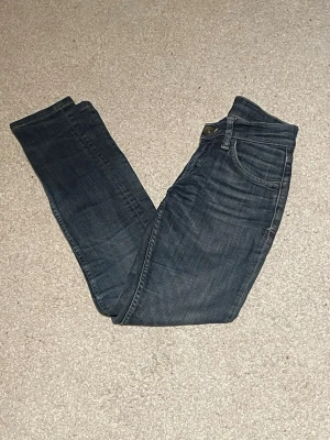 Tiger of Sweden blå jeans XS - Snygga blå jeans från Tiger of Sweden i storlek XS. Modellen har klassisk femficksdesign, raka ben och normal midja. Jeansen är i mörkblå tvätt med subtila slitningar och har en stilren patch bak i midjan. Perfekta till sneakers eller boots.