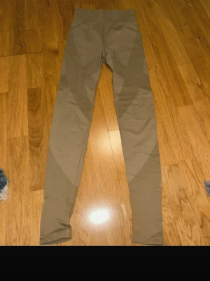 Beige ribbade leggings med hög midja - Snygga beige leggings med ribbade detaljer och hög midja. De har en tight passform och är tillverkade i ett stretchigt syntetmaterial som sitter skönt på kroppen. Perfekta för träning eller chill dagar. Inga fickor eller dragkedjor.