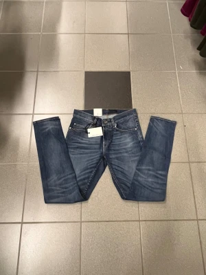 Blå tiger of sweden jeans W29 L32 - Snygga blå jeans från Tiger of sweden med straight leg och smal fot. Klassisk femficksmodell med bruna detaljer vid linningen och slitningar på benen för en cool look. Perfekt passform för dig som gillar stilrena jeans med lite edge.