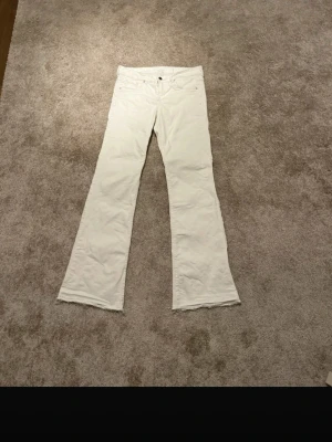 Vita bootcut jeans med rå kant - Snygga vita lågmidjade jeans med bootcut-snitt och fransad rå kant längst ner. Klassisk femficksmodell med knapp och dragkedja framtill. Perfekta för dig som gillar en lite retro och avslappnad stil. Materialet är jeans och färgen är helt vit.