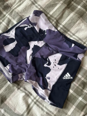 Adidas mönstrade träningsshorts - Säljer ett par Adidas träningsshorts med coolt abstrakt mönster i mörkblått och lila. De är tighta, tillverkade i mjuk och stretchig polyester med Aeroready-teknologi. Perfekta för gymmet eller löpning. De är avklippta och sydda som man ser i sista bilden 