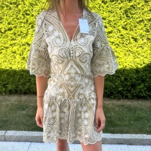 Beige spetsklänning från Sandro - Superfin kortklänning från Sandro i beige med vit broderad spets och blommigt mönster. Nypris 3500kr