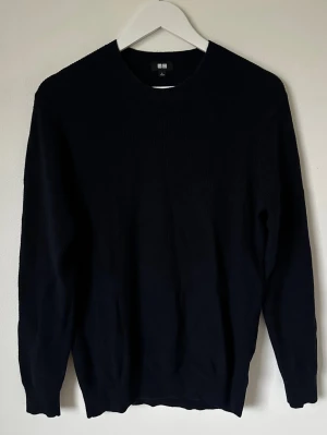 Mörkblå stickad tröja från Uniqlo - Mörkblå stickad tröja från Uniqlo i storlek L. Tröjan har rund hals och är långärmad med ribbade muddar. Materialet är en mjuk blandning av bomull och kashmir, vilket gör den extra skön och stilren. Perfekt för dig som gillar enkel och clean look. 5L17