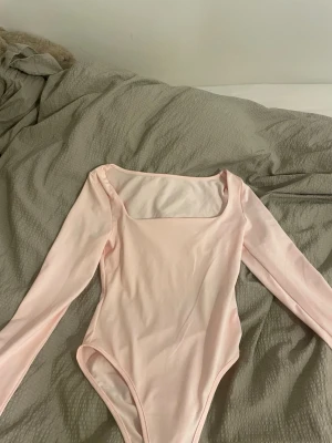 Ljusrosa långärmad body från SHEIN - Säljer en ljusrosa långärmad body från SHEIN i storlek XS. Toppen har en snygg fyrkantig urringning och är figurnära i modellen. Materialet är mjukt och stretchigt, perfekt att styla med jeans eller kjol för en clean look.
