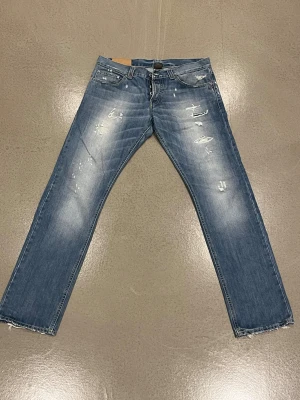 Blå distressed jeans från Dondup - Säljer ett par blå jeans från Dondup med snygga slitningar och blekta detaljer. Modellen har klassisk femficksdesign, knappgylf  och har en cool, lite ruffad look som passar perfekt till sneakers.