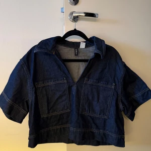 Mörkblå denim topp  - Säljer en mörkblå overshirt/ topp i denim med två stora fickor framtill och korta ärmar. Super fin topp som dock aldrig kommit till använd då jag redan har en liknade. Passar super bra till blåa jeans eller svarta kostymbyxor.