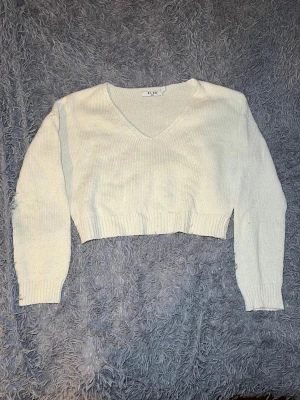 Vit/beige croppad stickad tröja NA-KD - Säljer en vit croppad stickad tröja från NA-KD i storlek S. Tröjan har v-ringad hals och långa ärmar med ribbade muddar. Perfekt för lager-på-lager och passar till jeans eller kjol. Enkel och stilren design som funkar året runt.
