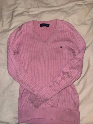 Rosa v-ringad tröja Tommy Hilfiger - Säljer en rosa v-ringad tröja från Tommy Hilfiger i storlek S. Tröjan är kabelstickad i 100% bomull och har långa ärmar samt en liten logga broderad på bröstet. Fint skick! Säljer pga används inte längre! 💕 Hör av er om frågor eller funderingar!💕💕Pris kan diskuteras vid snabb affär.