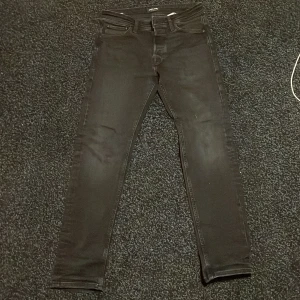 Svarta jeans från Jack & Jones - Säljer ett par svarta jeans från Jack & Jones med tapered passform. Modellen heter Mike och har klassisk femficksdesign, bälteshällor och dragkedja. Jeansen är tillverkade i stretchigt denim för extra komfort och har en snygg, mörk tvätt.