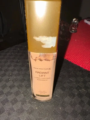 Max Factor Radiant Lift Foundation - Max Factor Radiant Lift Foundation i nyansen 80 Deep Bronze. Flytande foundation med långvarig lyster och SPF 30. Kommer i en rektangulär glasflaska med guldfärgat lock. Ger all-day hydration och en strålande finish.